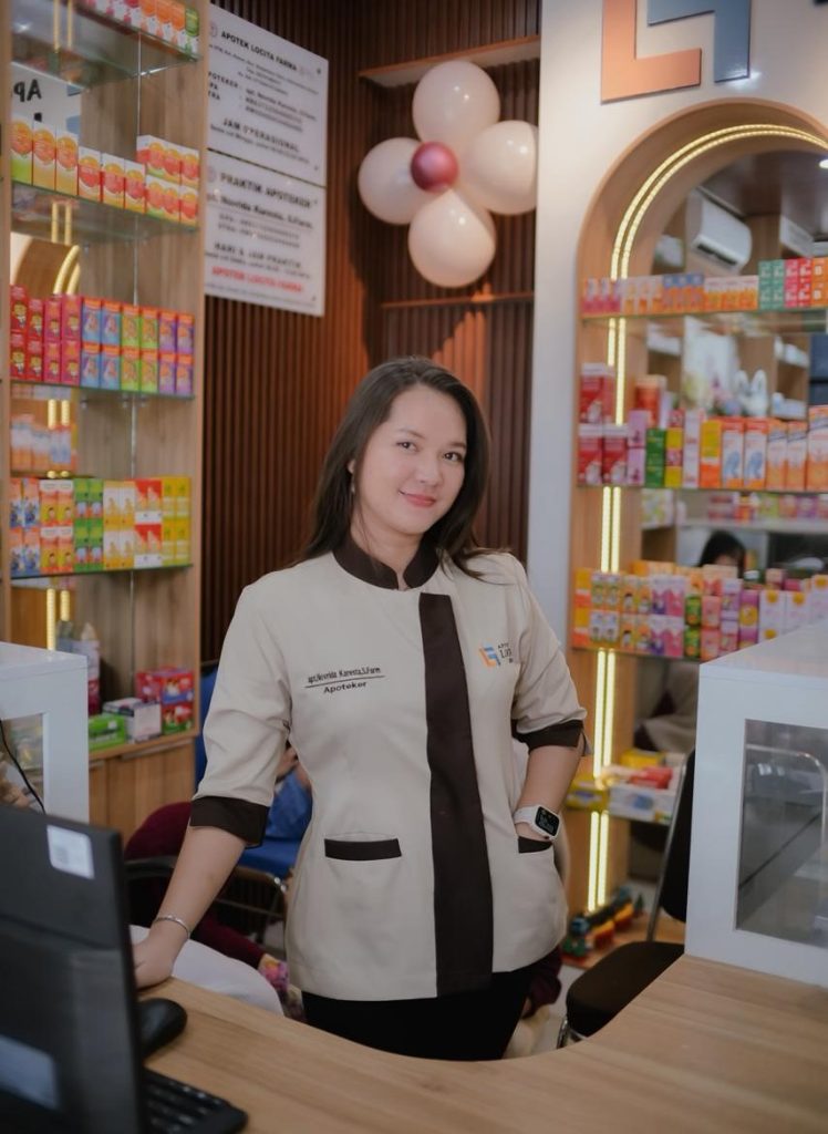 apoteker locita farma berdiri di kasir dengan aplikasi apotekernet